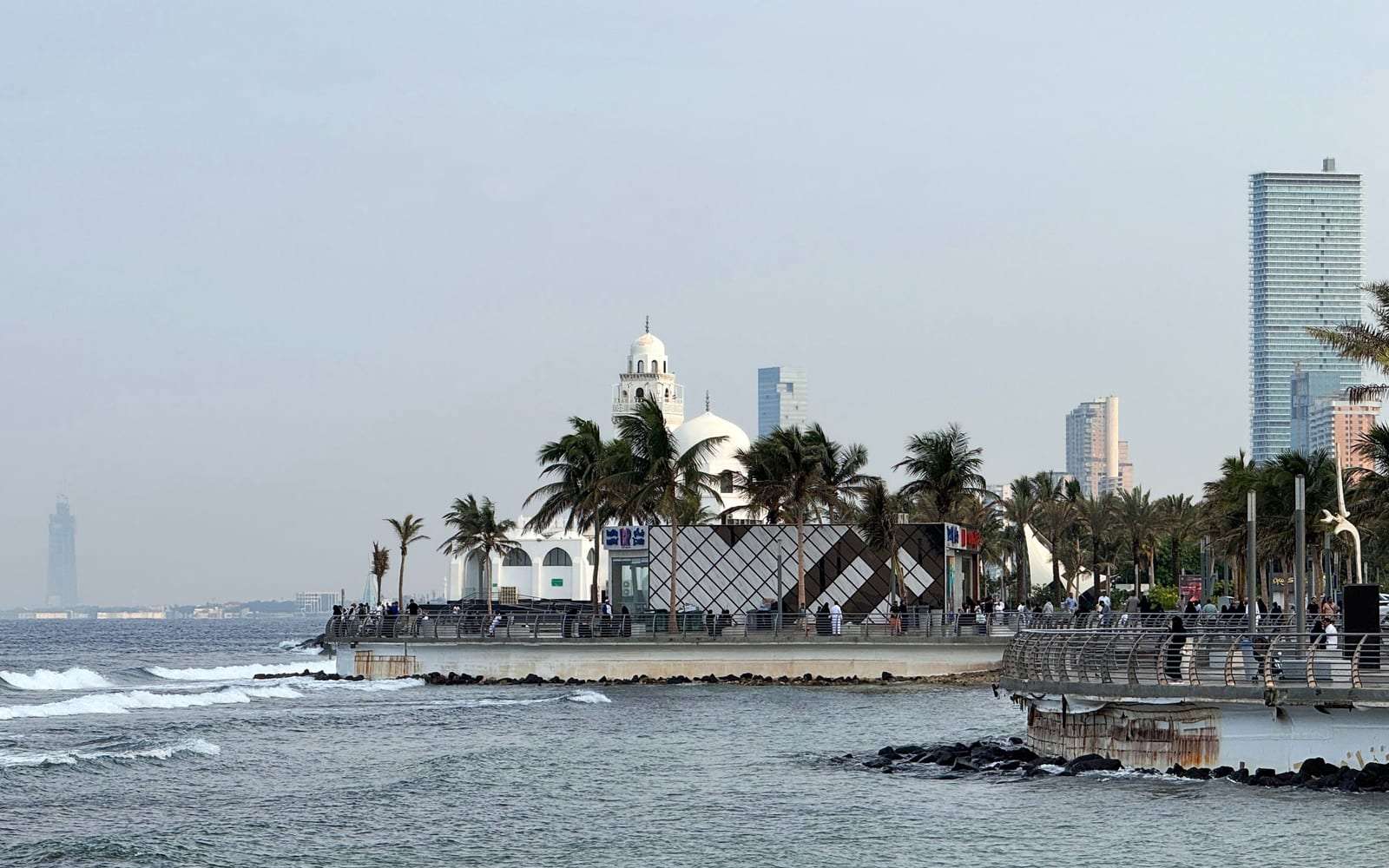 كورنيش جدة على البحر الأحمر بمسجد أبيض ونخيل ومبانٍ في الأفق